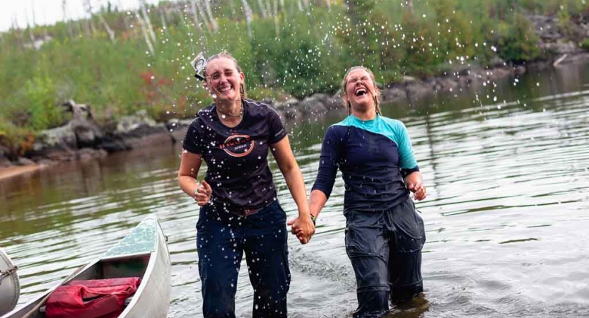 two people standing knee-deep in water hold hands and laugh after being splashed